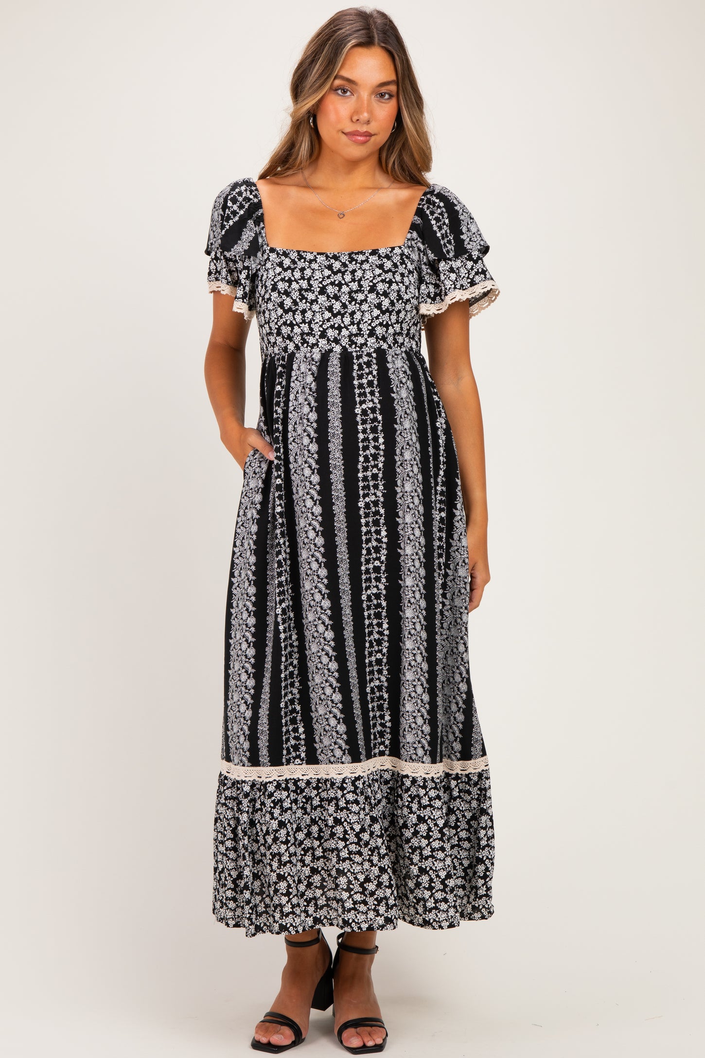 woman wearing a black and white floral print maternity dress with short ruffle sleeves and pockets, featuring a fitted bodice and flowing skirt