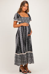 woman wearing a black floral print maternity dress with short sleeves and a square neckline, holding her baby bump