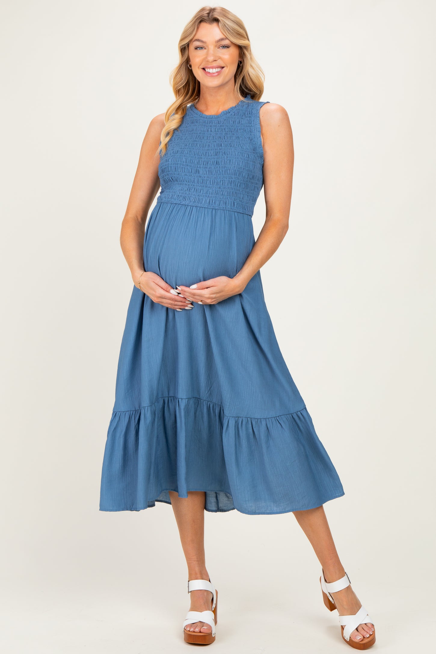 woman wearing a blue maternity dress with smocked bodice and tiered skirt, holding her baby bump