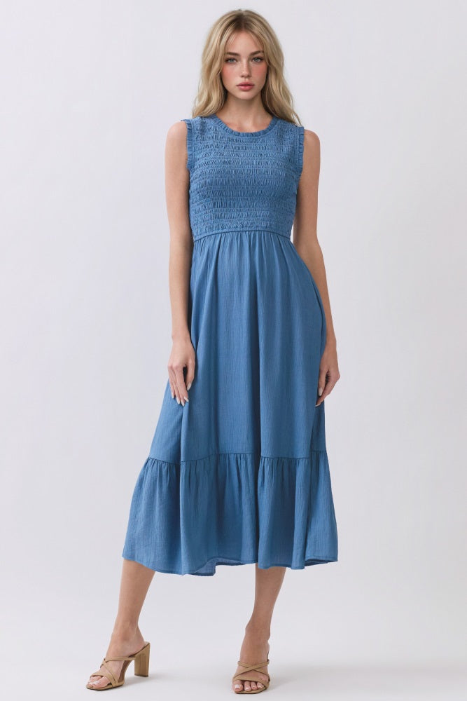 woman wearing a blue sleeveless midi dress with smocked bodice and tiered skirt, standing in a neutral background