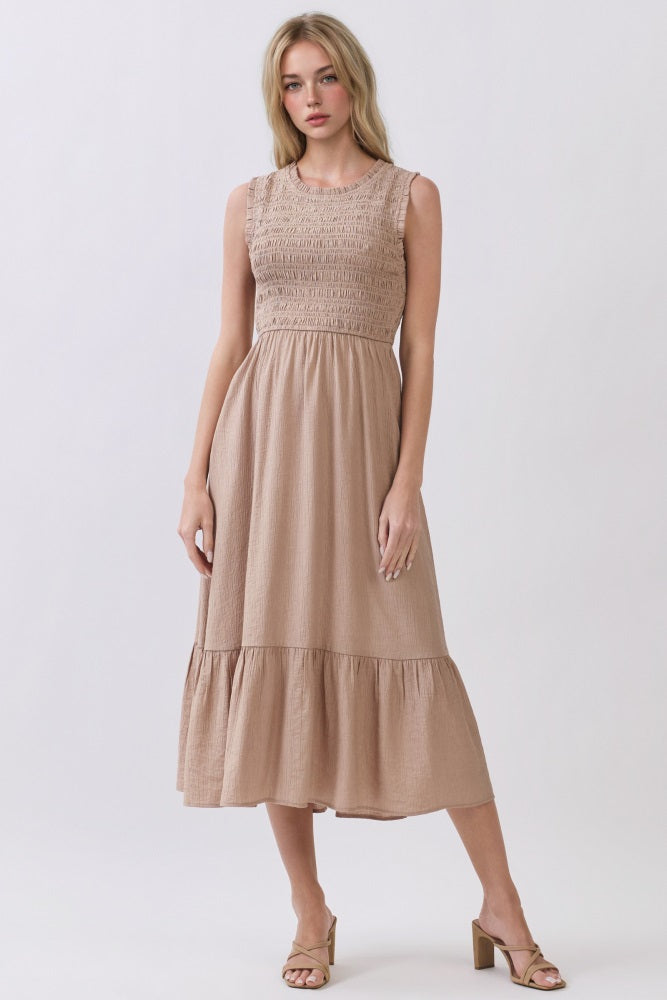 woman wearing a beige sleeveless maxi dress with smocked bodice and flared skirt, standing on a light background