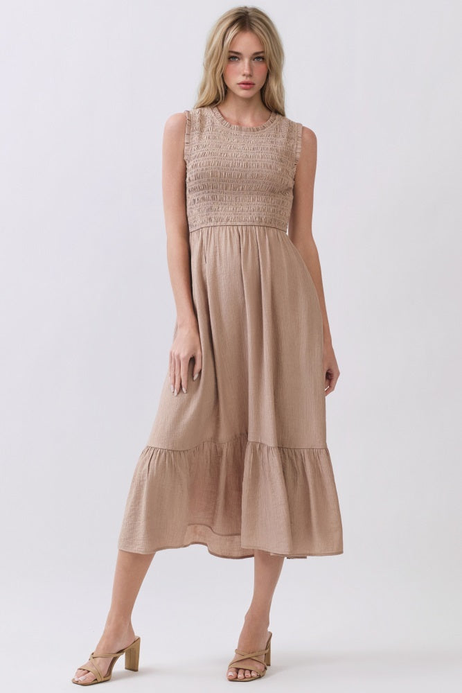 woman wearing a beige sleeveless midi dress with smocked bodice and tiered skirt, paired with heeled sandals