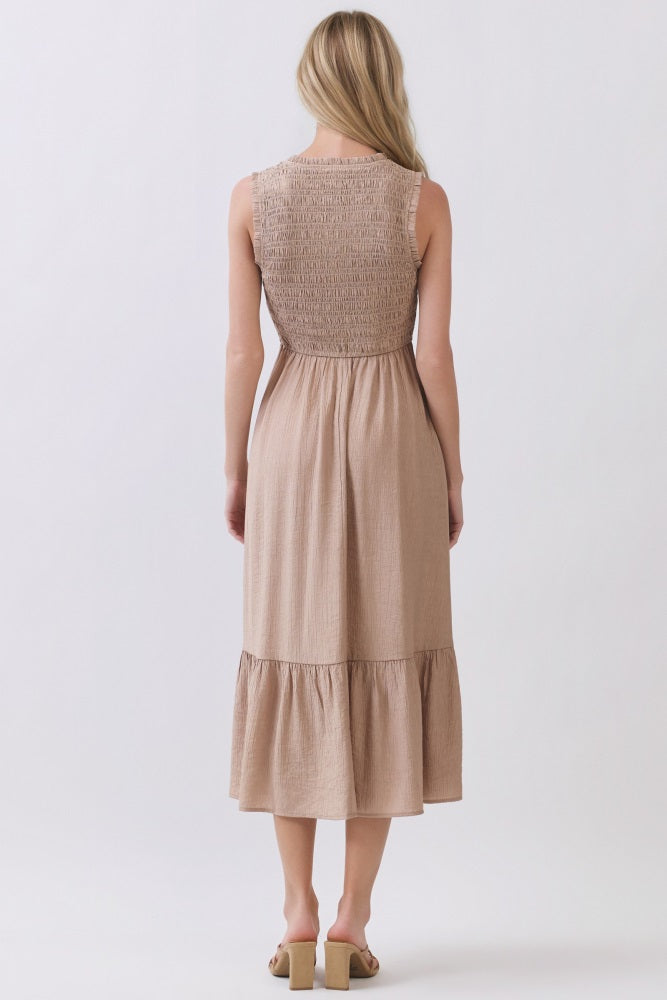 woman wearing a tan sleeveless dress with a smocked back and tiered hem, viewed from the back