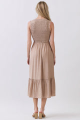 woman wearing a tan sleeveless dress with a smocked back and tiered hem, viewed from the back