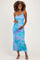 woman wearing a blue and purple floral maternity dress, gently cradling her baby bump