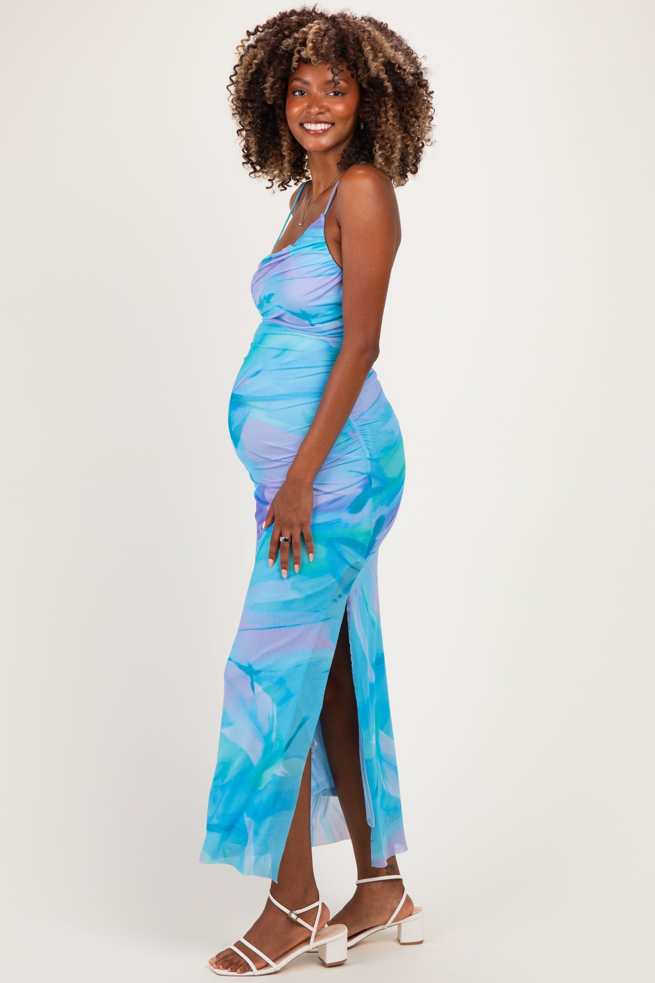 woman wearing a blue tropical print maternity dress with side slit and ruching, showcasing her baby bump