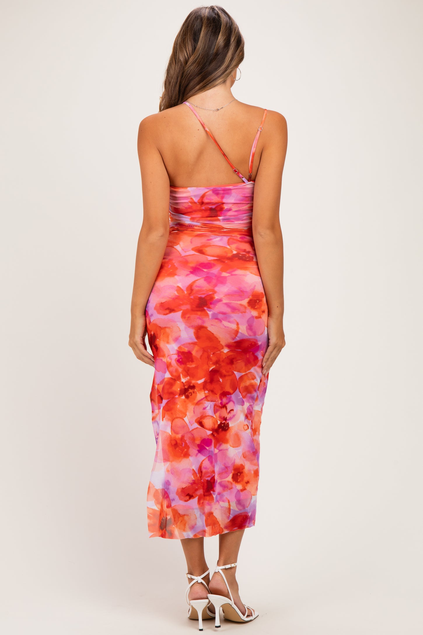 woman wearing a floral maternity dress with a fitted silhouette and spaghetti straps, showing a colorful pink and orange pattern