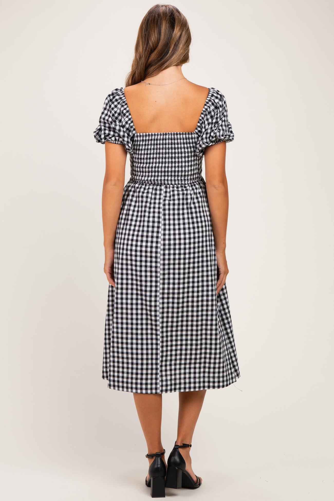woman wearing a black and white gingham maternity dress with puff sleeves and a fitted bodice, showing a baby bump