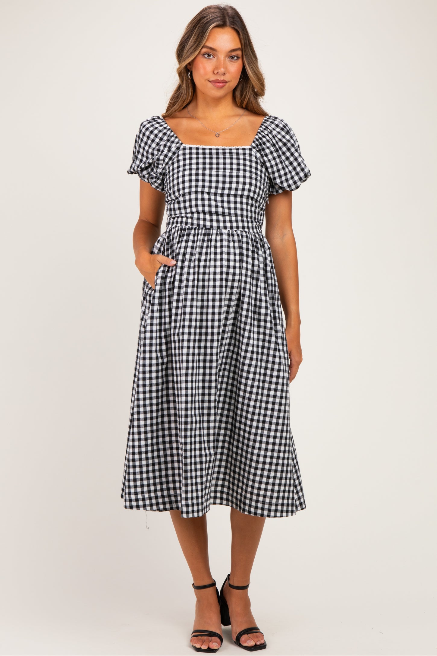 woman wearing a black and white gingham maternity dress with short puff sleeves and pockets, showing a baby bump