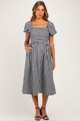 woman wearing a black and white gingham maternity dress with short puff sleeves and pockets, showing a baby bump