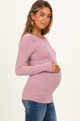 woman wearing a mauve ribbed maternity top and showing her baby bump while posing to the side
