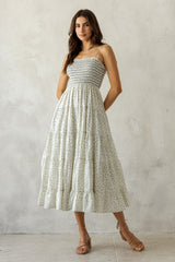 woman wearing a white floral maxi dress with thin straps and a smocked bodice, standing against a neutral backdrop