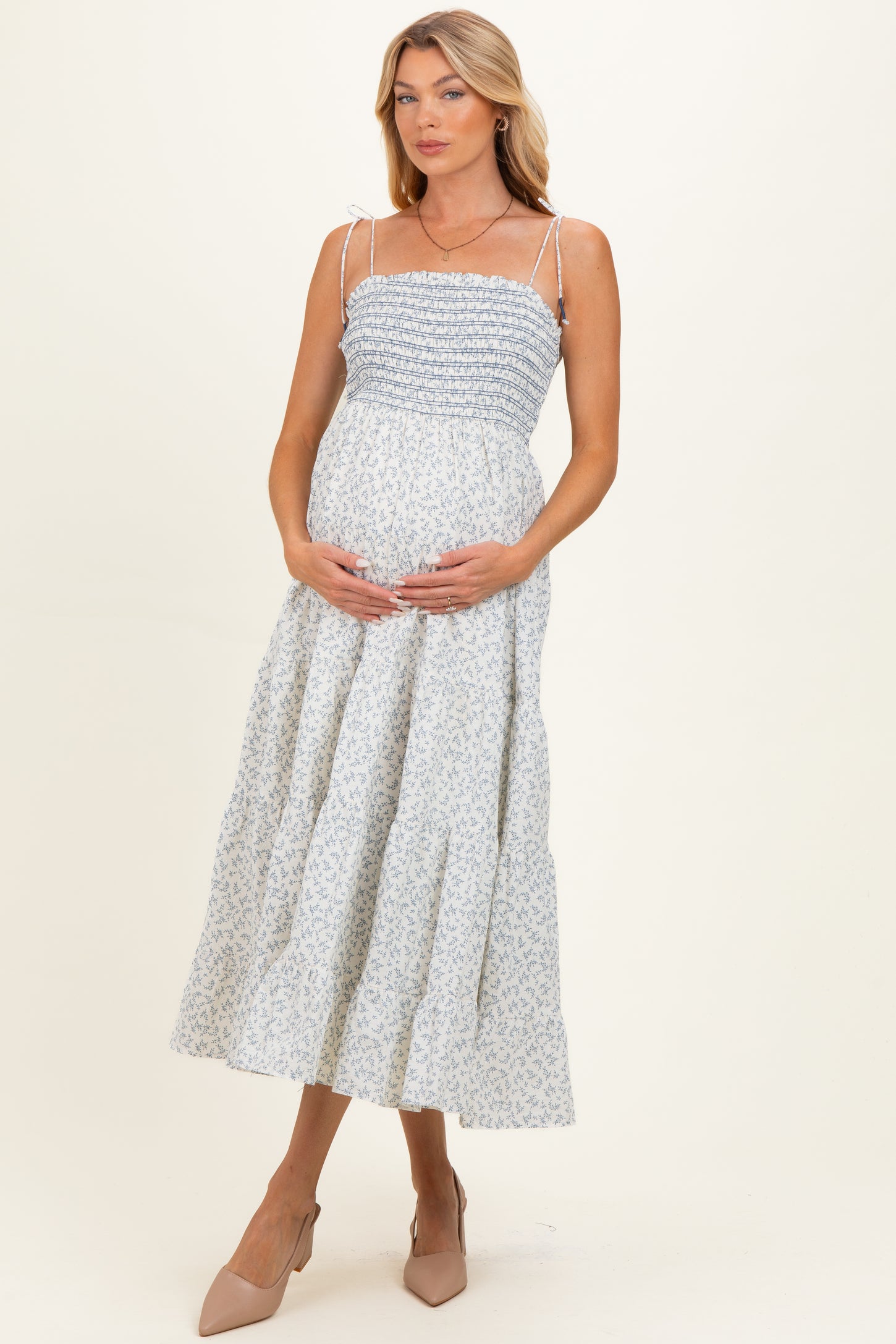 woman wearing a light blue floral maternity maxi dress and cradling her baby bump