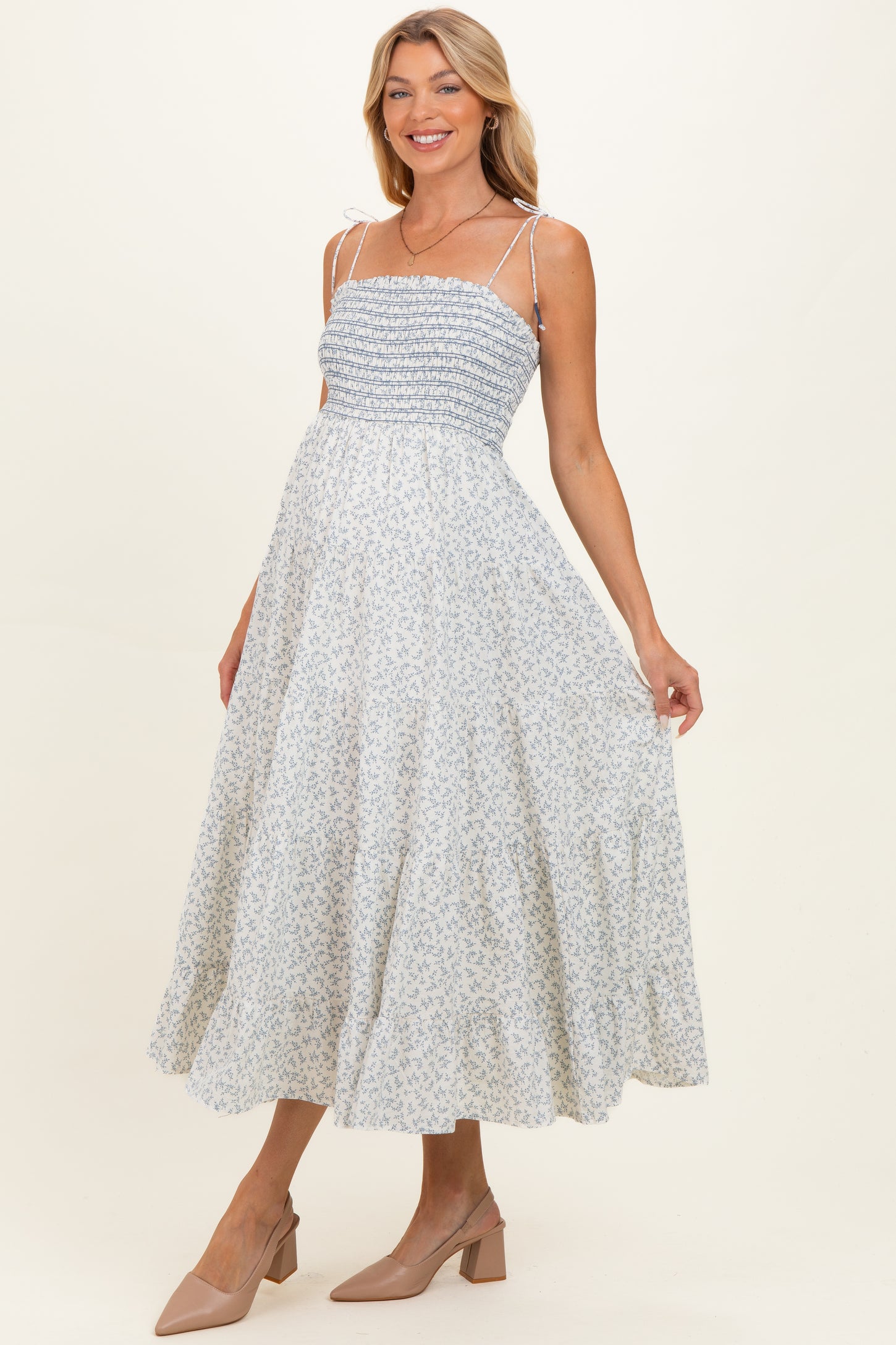 woman wearing a light blue floral maternity dress with smocked bodice and adjustable straps, holding her baby bump