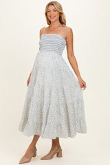 woman wearing a light blue floral maternity dress with smocked bodice and adjustable straps, holding her baby bump