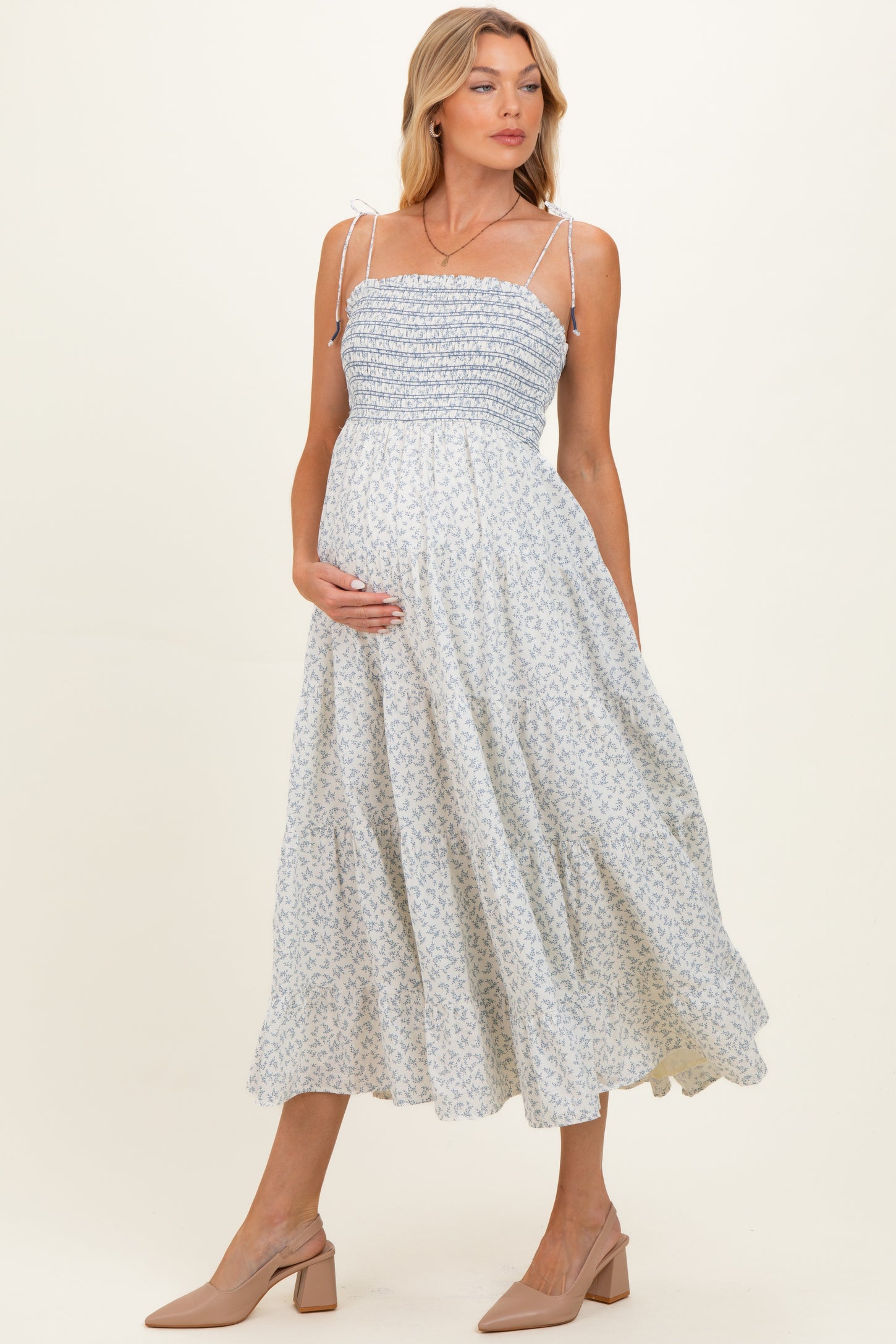 woman wearing a light blue floral maternity dress with smocked bodice and spaghetti straps, showing her baby bump