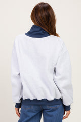 woman wearing a gray oversized sweatshirt with a navy collar and cuffs, facing away from the camera