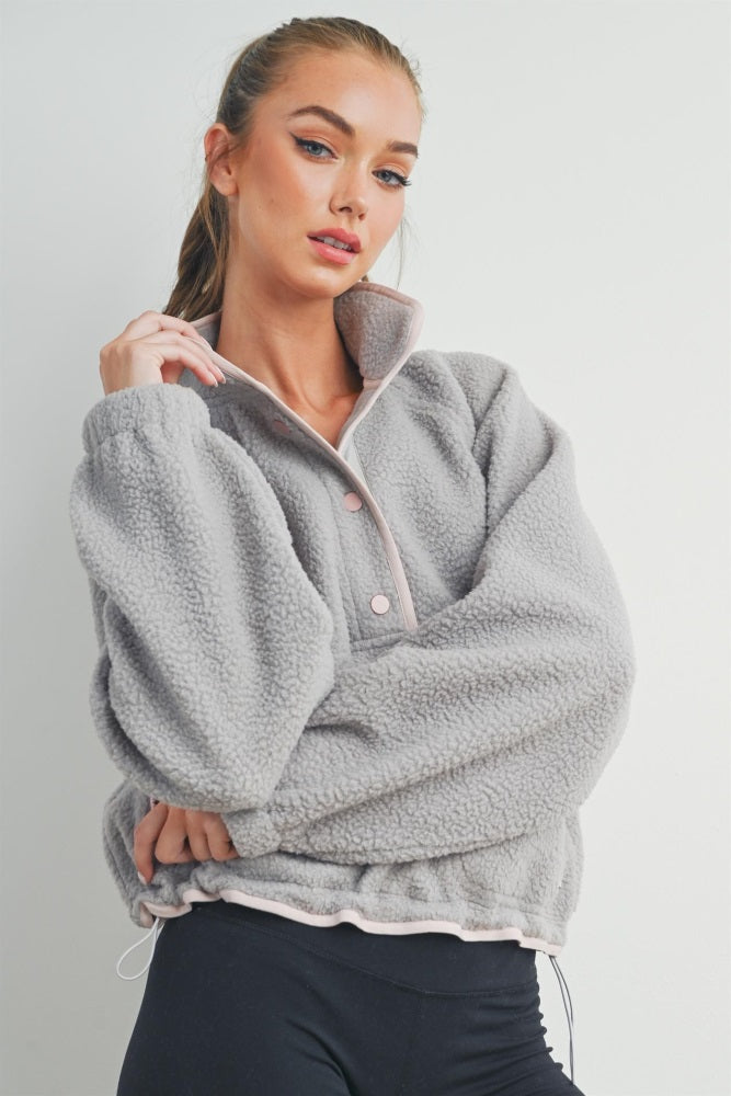woman wearing a gray fleece pullover jacket with a zip collar and pink detailing, posing with one hand on her hip