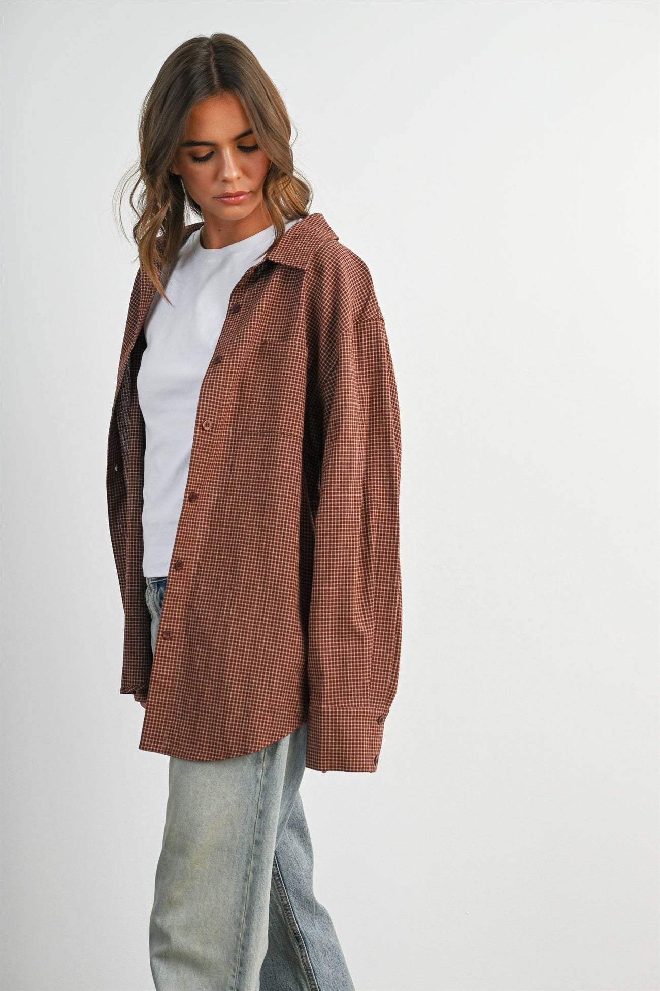 woman wearing a brown and white checkered oversized button-up shirt with a white t-shirt and light blue jeans