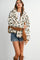 woman wearing a cream floral patterned fuzzy jacket with brown accents, paired with denim shorts and tall brown boots