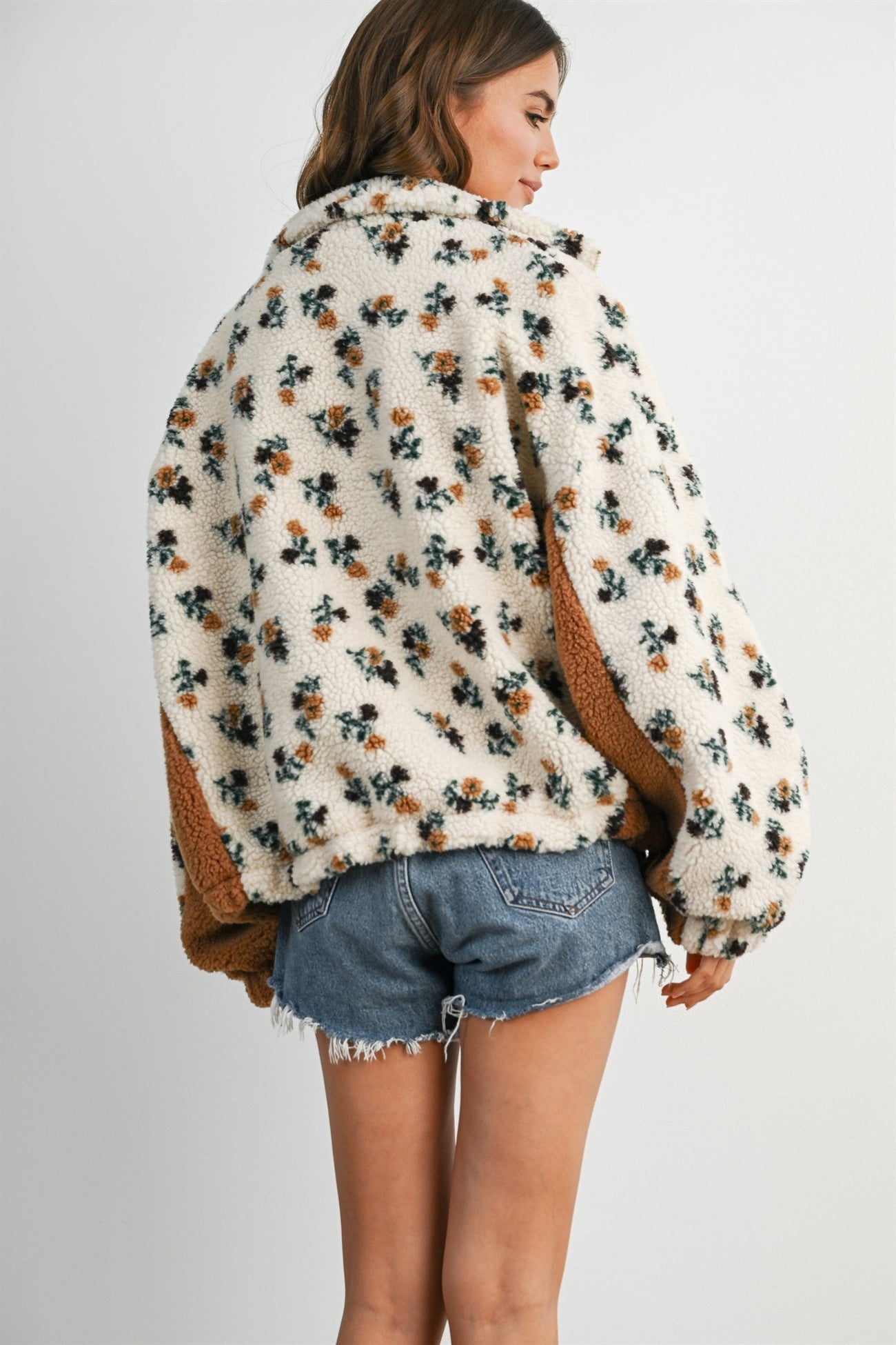 woman wearing a cream floral patterned oversized fleece jacket with orange accents paired with denim shorts