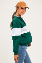 woman wearing a green and white striped maternity sweatshirt with a visible baby bump and a brown cap