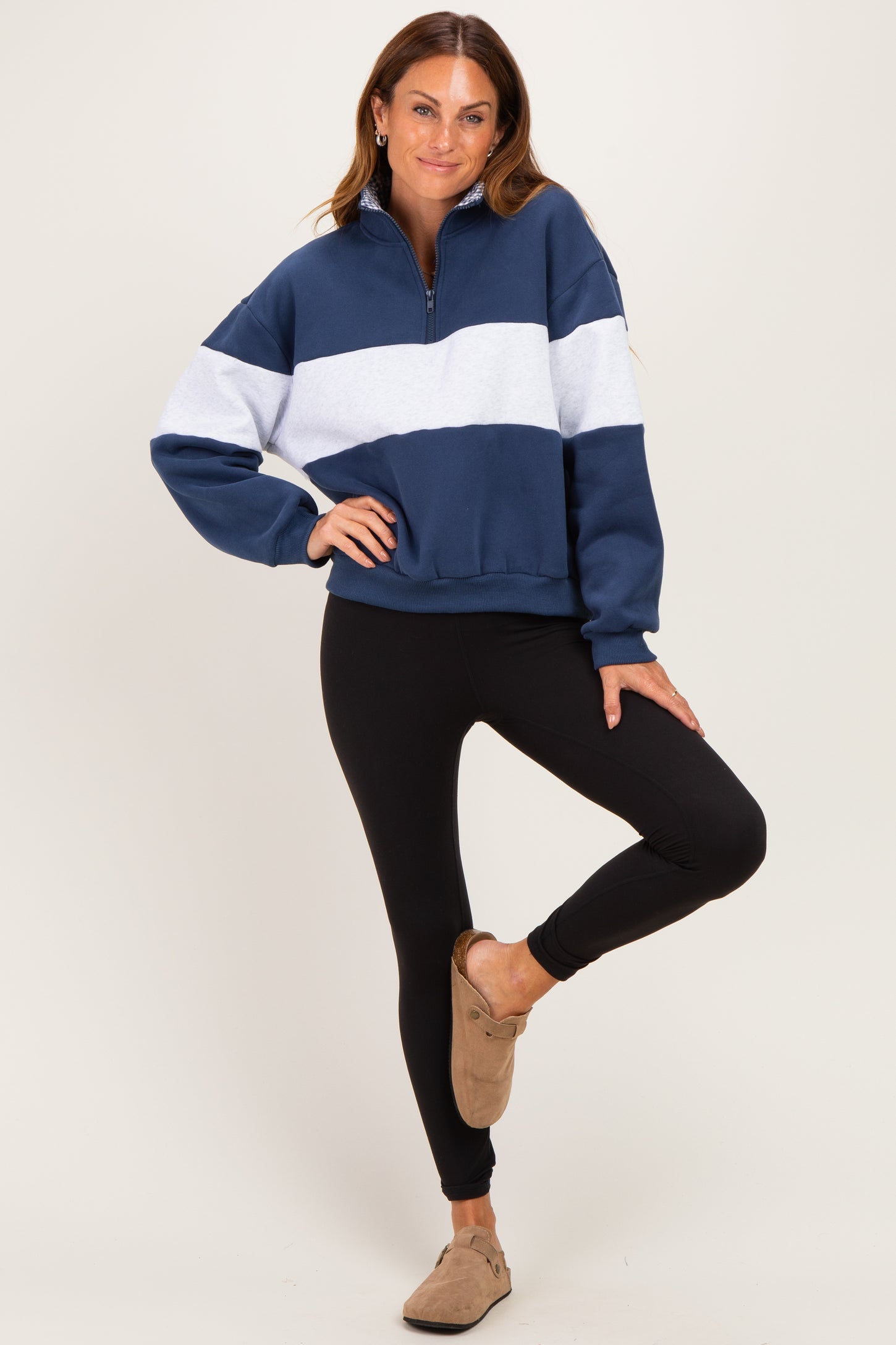 woman wearing a navy blue and white color block half-zip pullover sweatshirt with black leggings and slip-on shoes