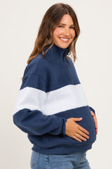 woman wearing a navy blue and gray striped quarter-zip maternity sweatshirt and cradling her baby bump