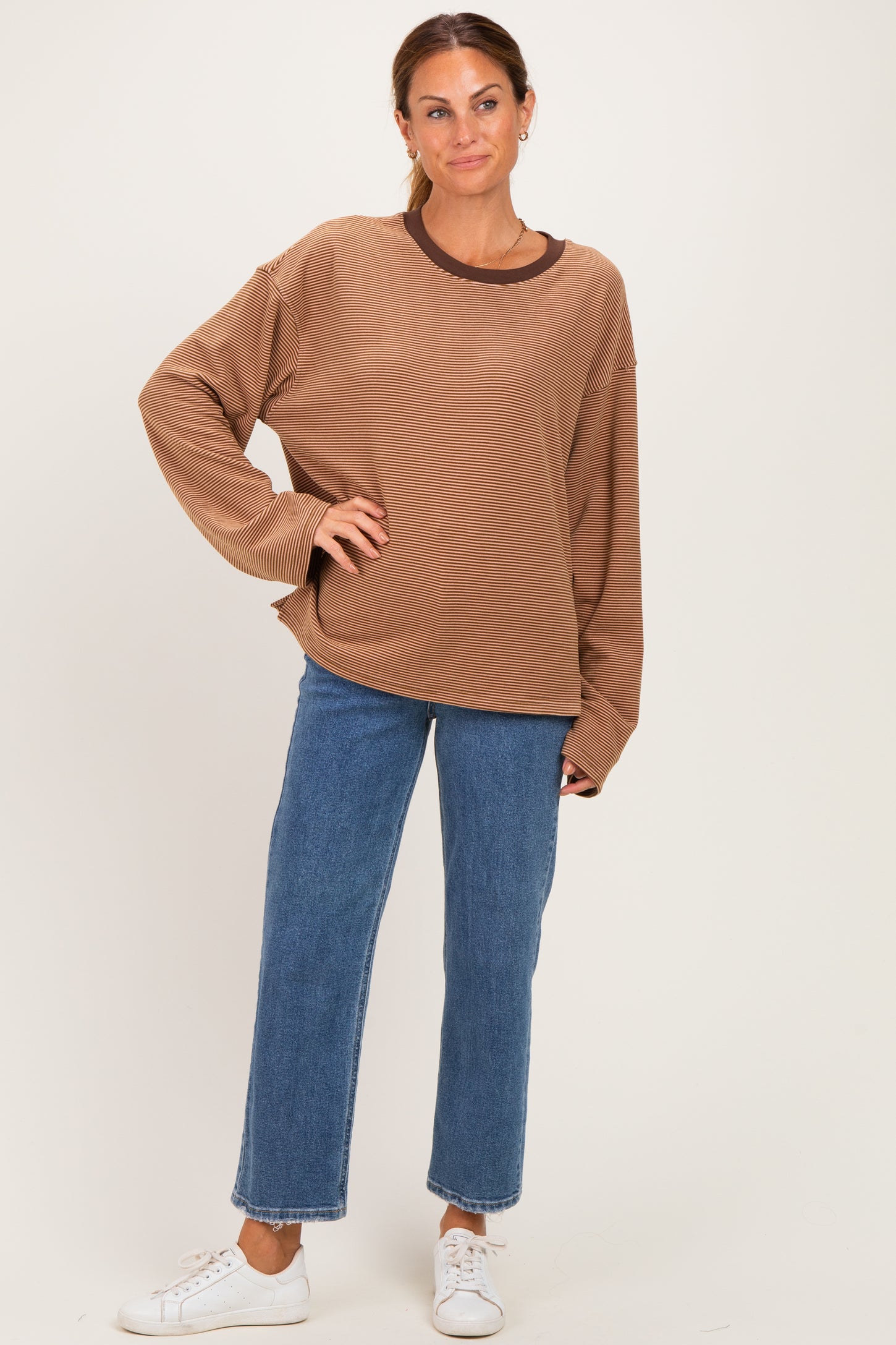 woman wearing a brown oversized sweater with a round neckline and long sleeves paired with light blue straight leg jeans