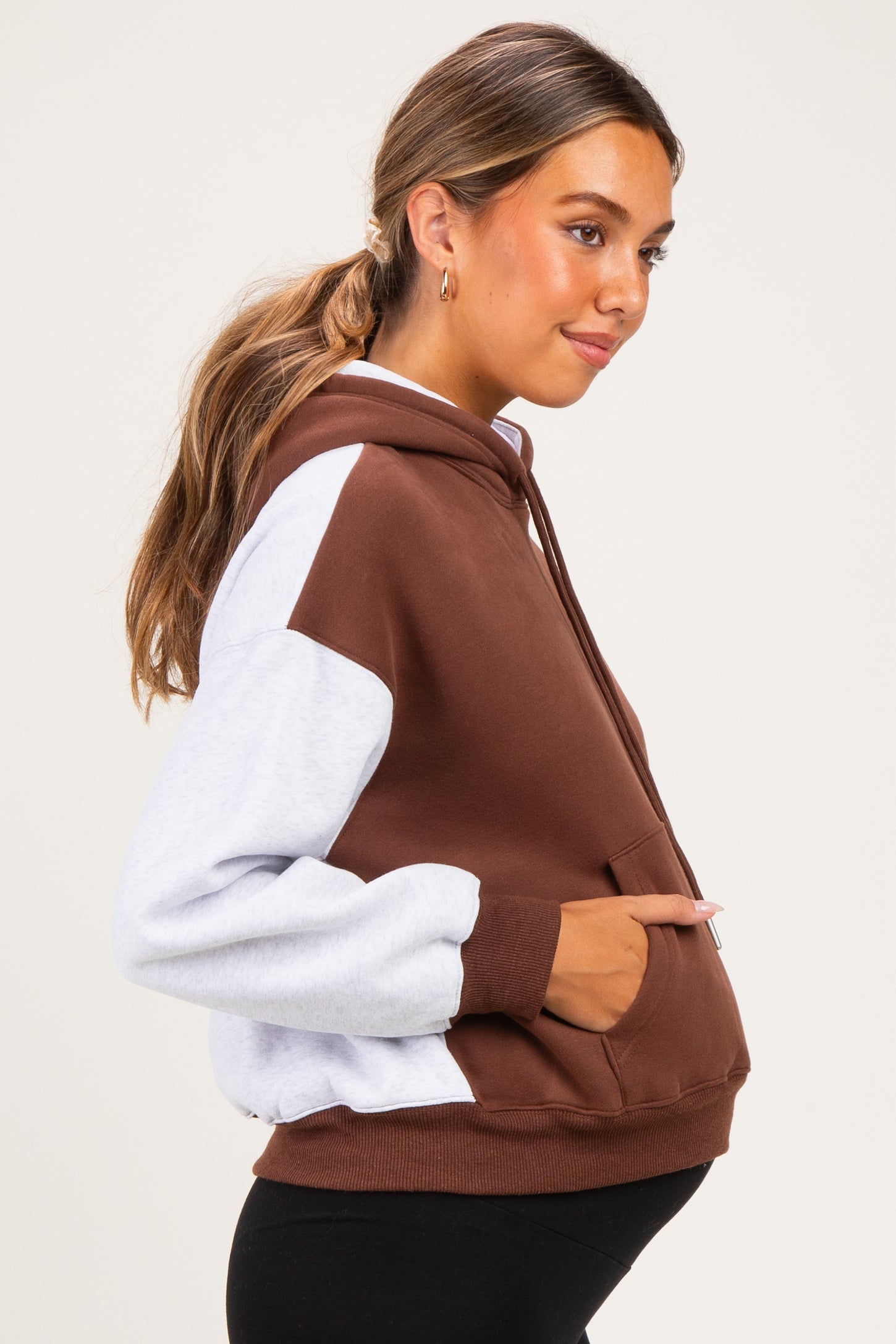 woman wearing a color-blocked maternity hoodie in brown and gray, with a visible baby bump