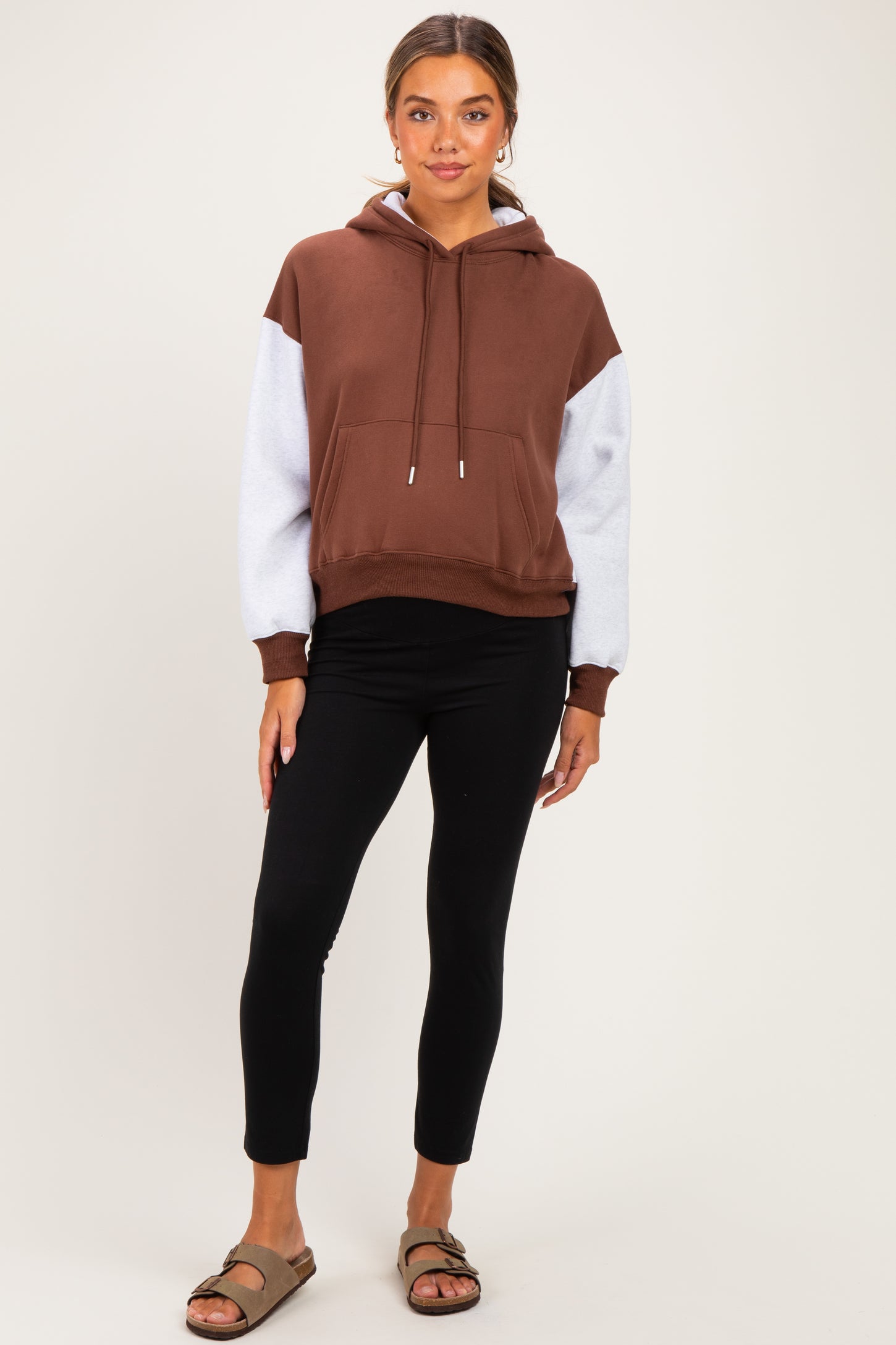 woman wearing a brown and gray color block maternity hoodie with a relaxed fit and black maternity leggings