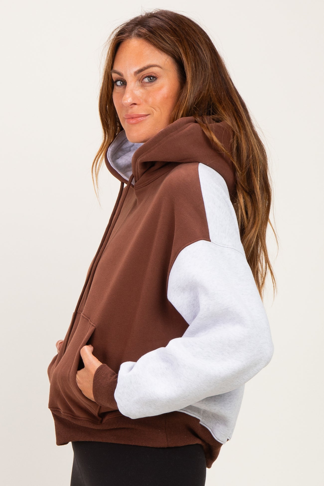 woman wearing a brown and gray color-block oversized hoodie with a front pocket and drawstring hood