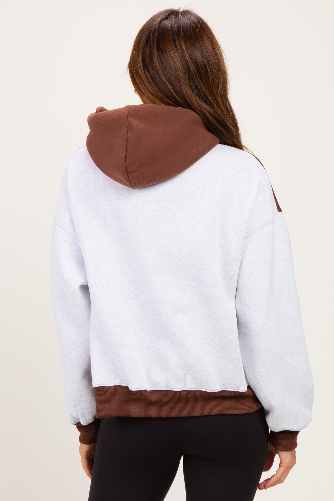 woman wearing a gray cropped hoodie with a brown hood and cuffs, seen from the back