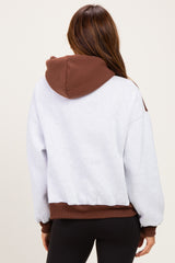 woman wearing a gray cropped hoodie with a brown hood and cuffs, seen from the back