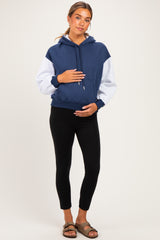 woman wearing a color-blocked navy and gray maternity hoodie, holding her baby bump and paired with black leggings