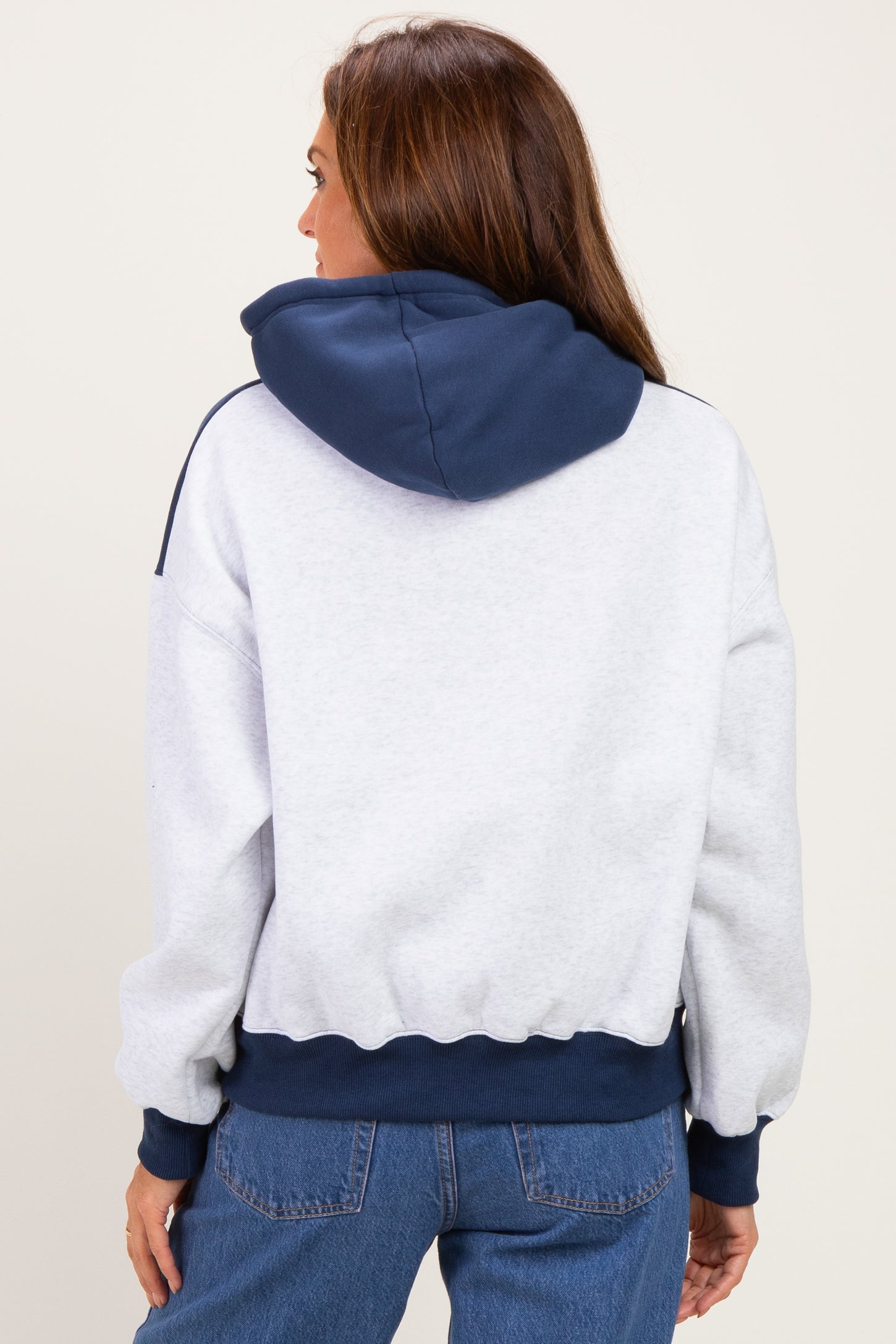 woman wearing a gray and navy hoodie with a cropped fit and ribbed cuffs, seen from the back