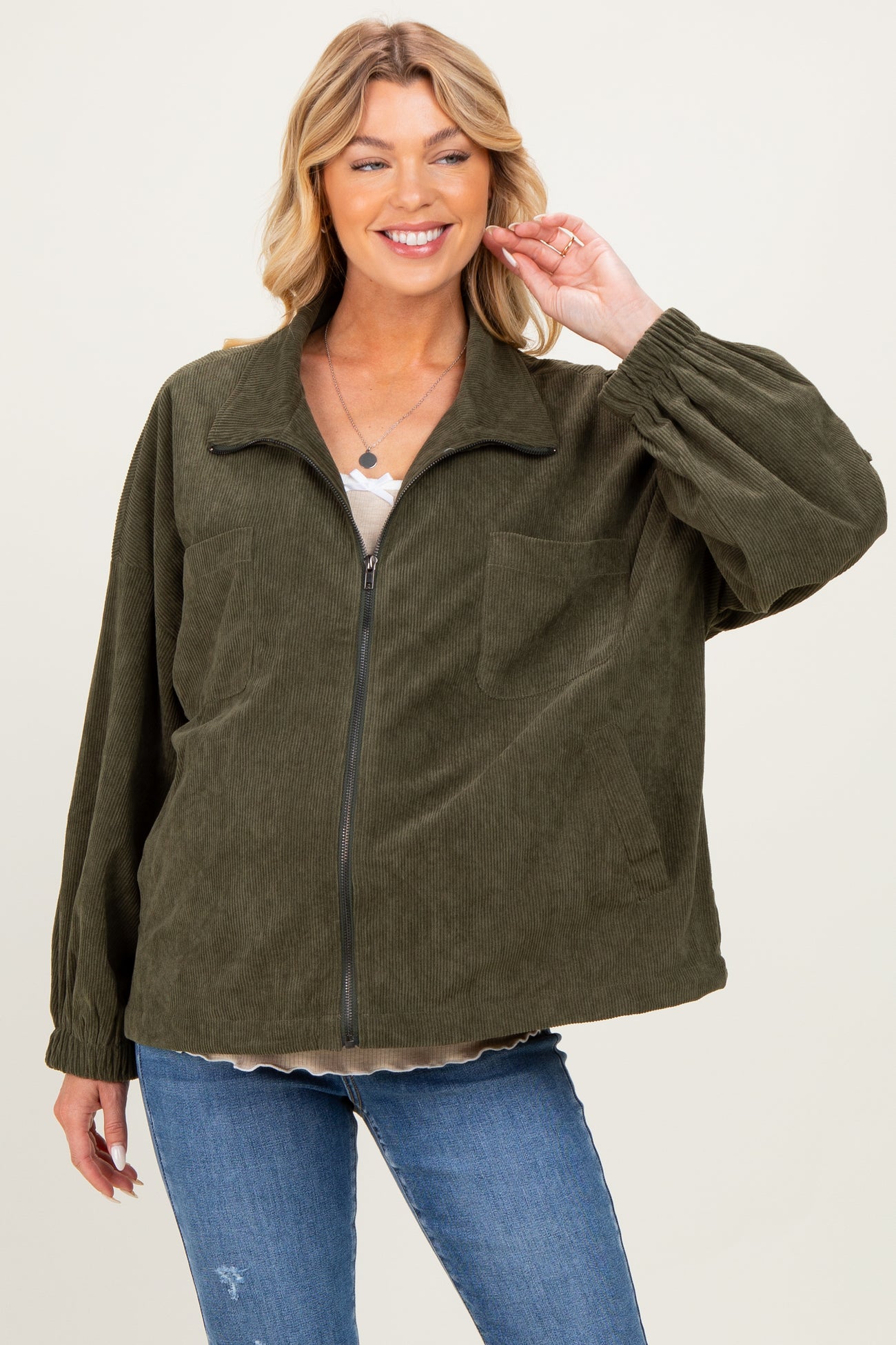 woman wearing a dark green corduroy zip-up jacket with balloon sleeves and front pockets over a beige top and jeans