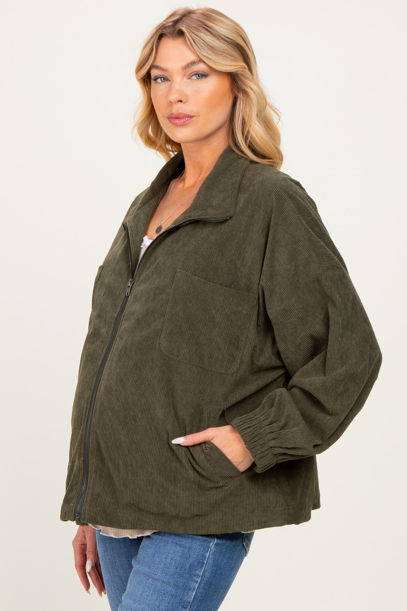 woman wearing a dark green corduroy maternity jacket with a oversized fit and front pocket, displaying her baby bump