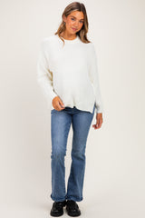 woman wearing a white knit maternity sweater and blue flared jeans, baby bump visible