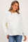 woman wearing a white knitted maternity sweater with a relaxed fit and side slits, paired with blue jeans and smiling