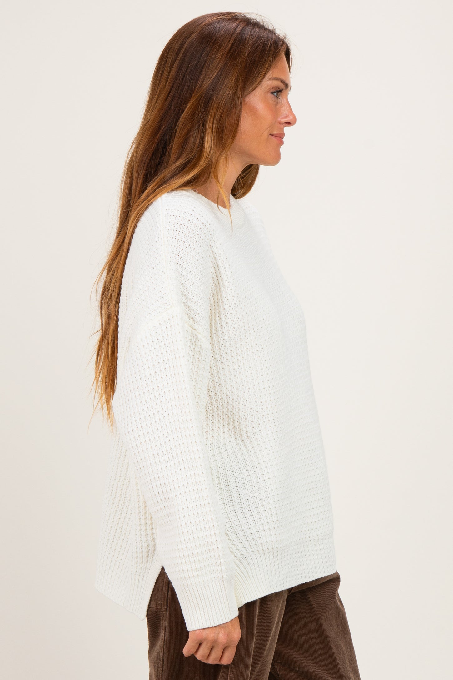woman wearing a white oversized knit sweater with a textured pattern and side slits, model shown from the side