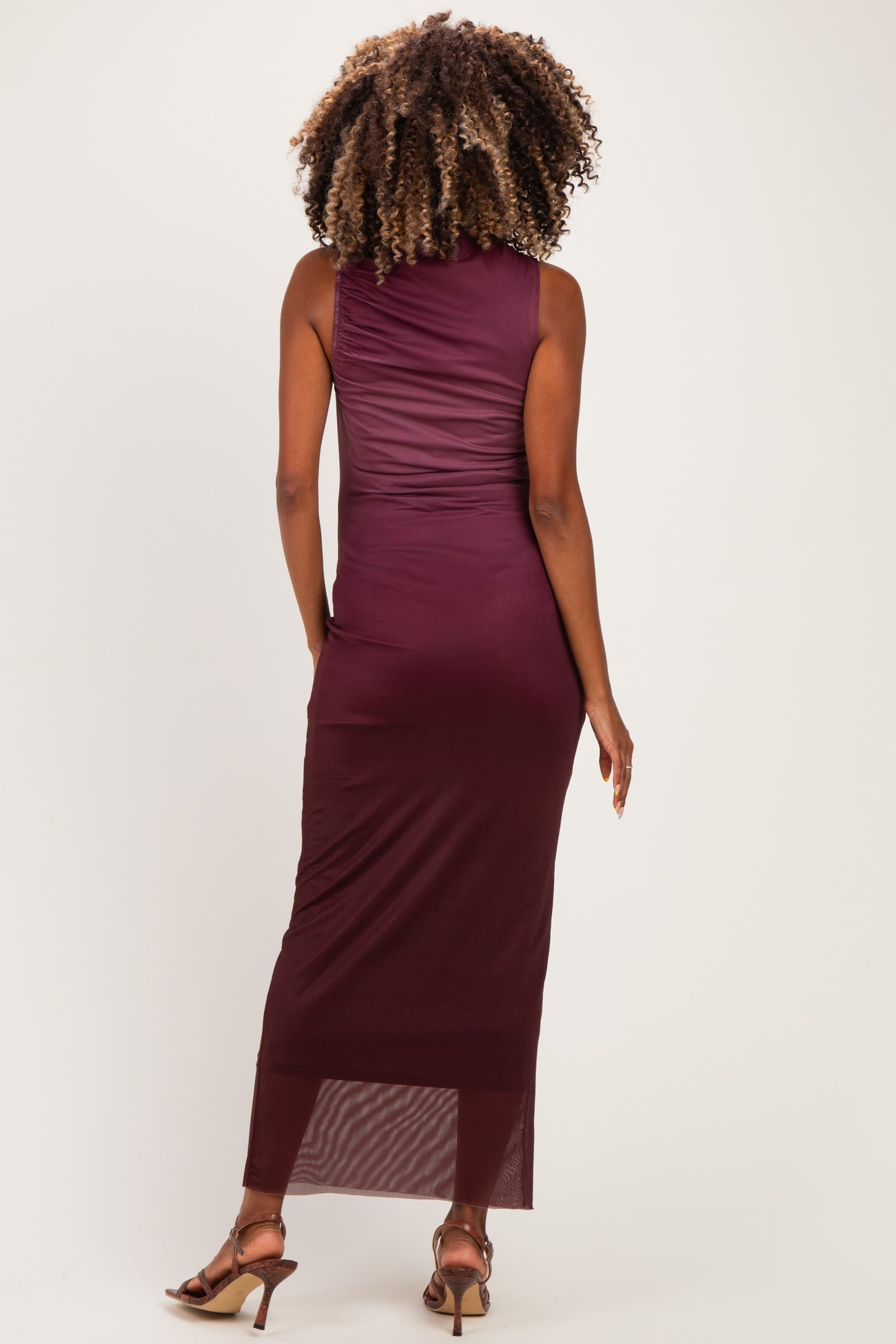 woman wearing a burgundy sleeveless maternity dress with a fitted silhouette and a long, sheer hemline