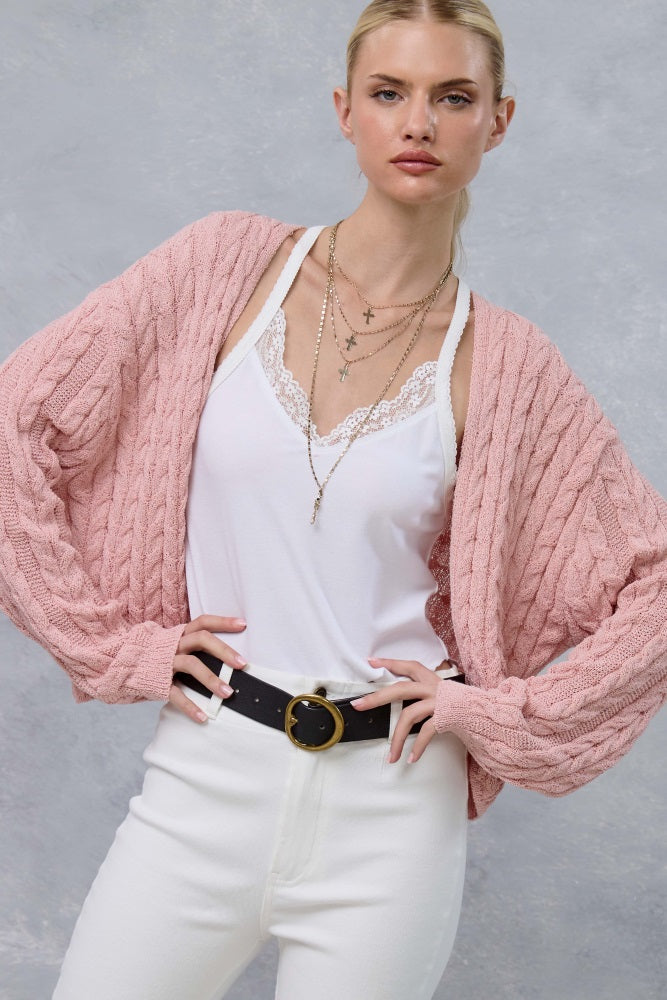 woman wearing a light pink oversized cable knit cardigan over a white lace camisole and white high-waisted pants