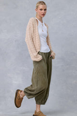 woman wearing a cream cable knit cardigan over a white tank top and olive green baggy pants, paired with tan slip-on shoes