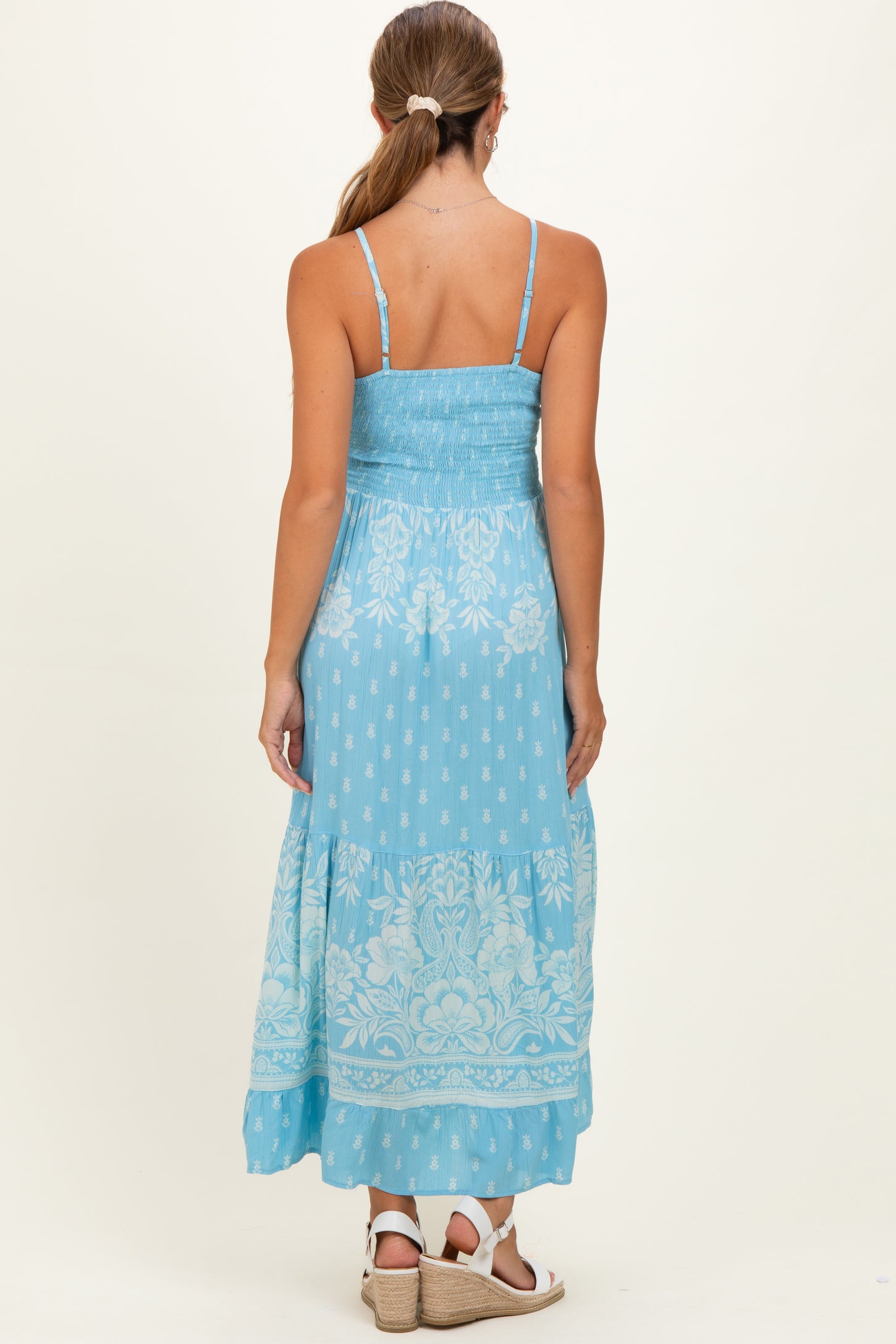 woman wearing a light blue maternity maxi dress with spaghetti straps and a tiered design, showing a baby bump from the back