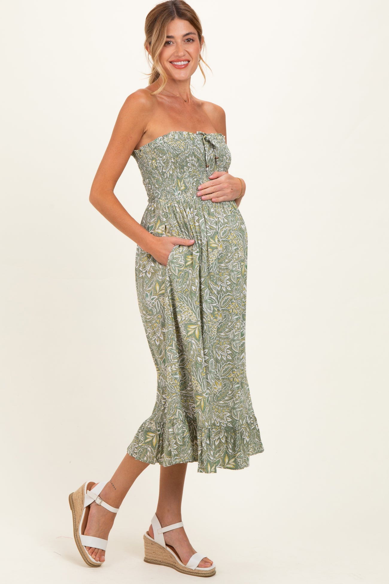 woman wearing a green floral strapless maternity dress with side pockets and a baby bump visible