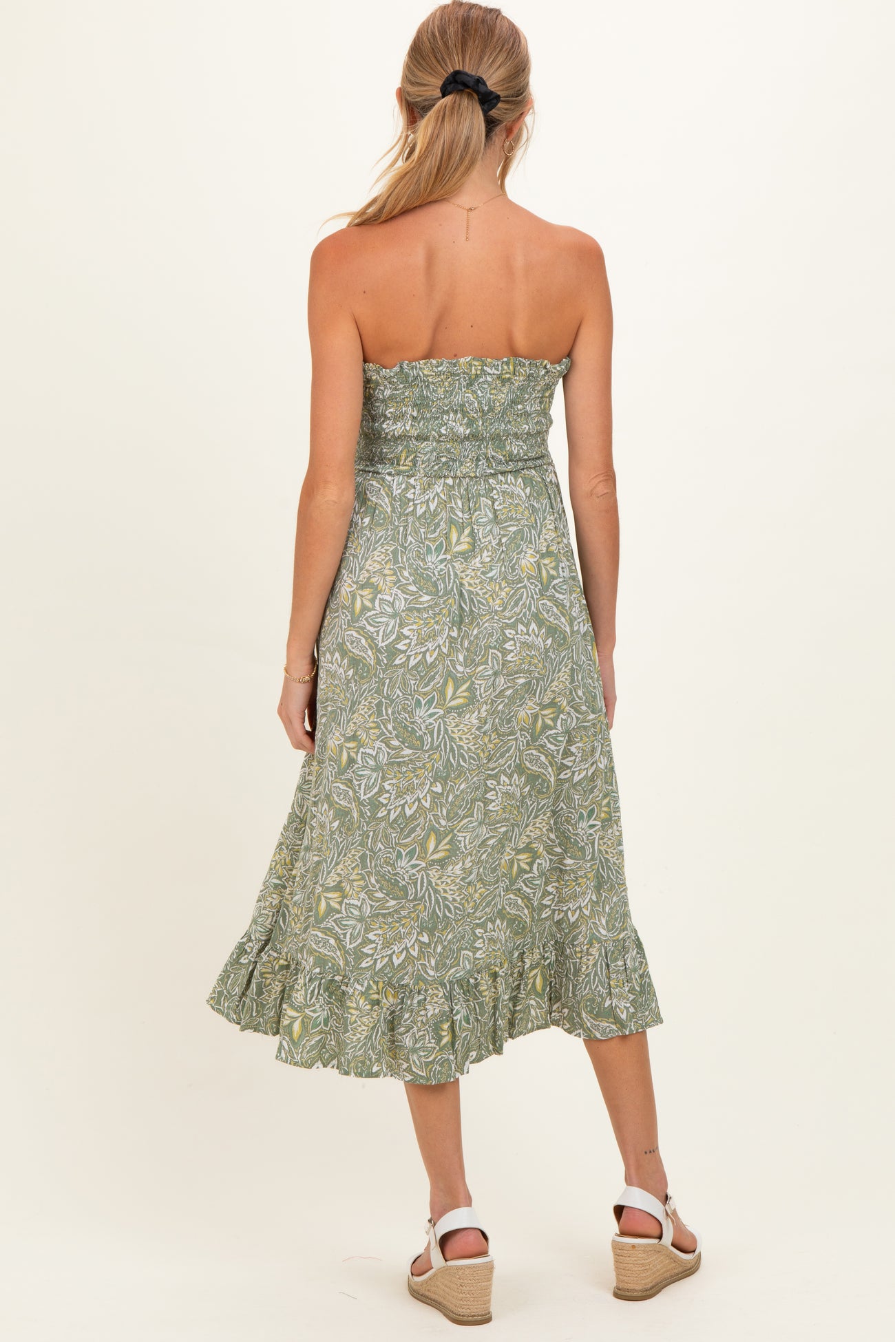 woman wearing a green floral print maternity dress with a smocked bodice and ruffled hem, showing her baby bump