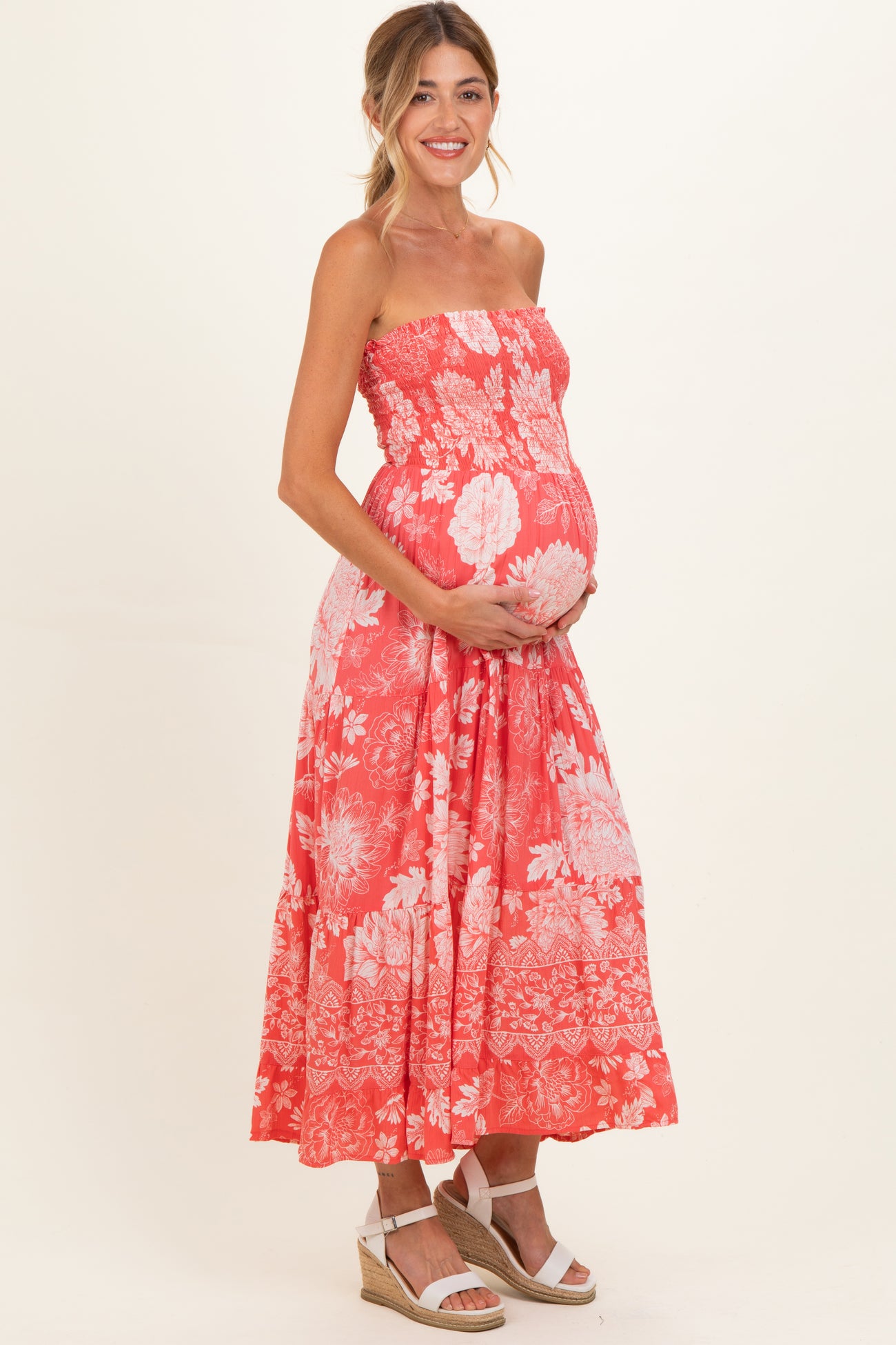 woman wearing a coral strapless maternity dress with floral print and holding her baby bump
