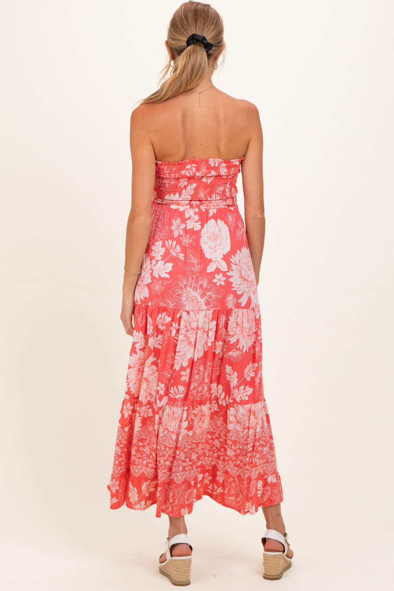 woman wearing a strapless coral floral maternity dress with a tiered skirt, showing her back