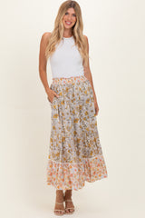 woman wearing a white sleeveless top and a long floral maxi skirt with pockets, standing with hands in skirt pockets
